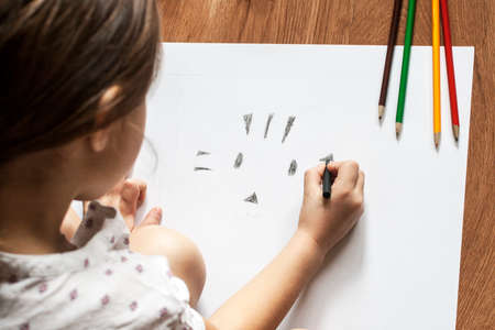 Girl draws picture with crayons on the sheet of paper on the floorの写真素材