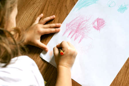 Girl draws picture with crayons on the sheet of paper on the floorの写真素材