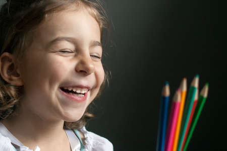 Girl sincerely laughing, looking at colored pencilsの写真素材