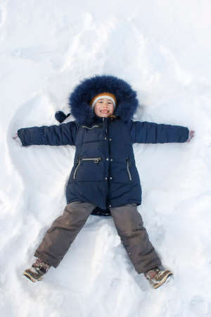 A girl in a blue jacket makes a snow angel lying on the snowの写真素材
