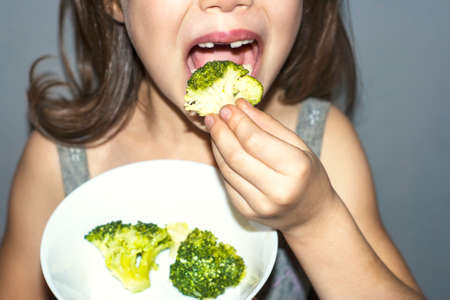 Baby girl eating cabbage broccoli with her handsの写真素材
