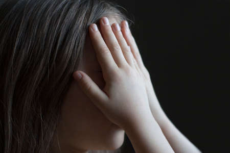 The face of a little girl, closed by handsの写真素材