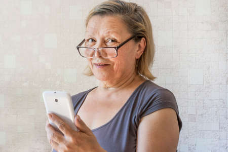 An elderly lady with a mobile phone in her hand looks at the camera through glassesの写真素材