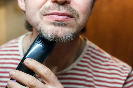 A middle-aged bearded man shaves trimmer. Close-upの写真素材