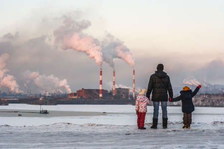 A man with children looks at a metallurgical plant polluting the atmosphereの写真素材
