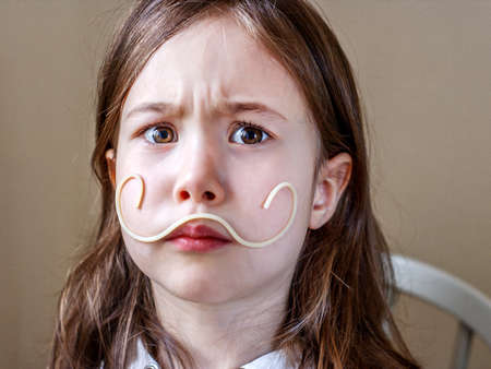 A child with spaghetti on his face depicts an Italian senor with a mustacheの写真素材