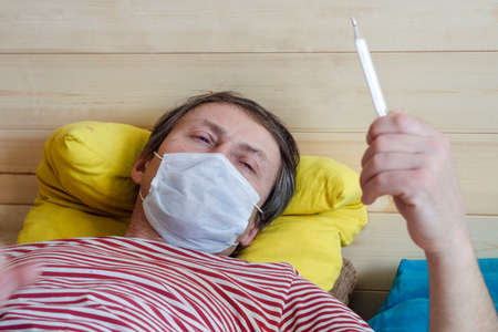 middle-aged man in a medical mask with a thermometer in his hand.の写真素材