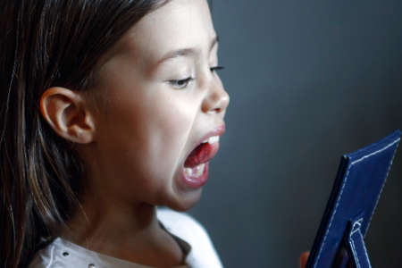 The girl in front of the mirror does logopedic exercises. Gymnastics for the tongueの写真素材