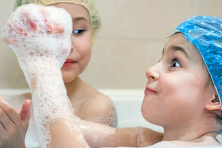 Little girls cheerfully takes a bath in the shower cap and plays with foamの写真素材
