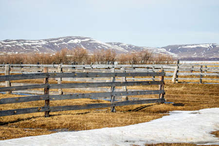 Rural landscape with a wooden fence and snow-capped mountains in the distance