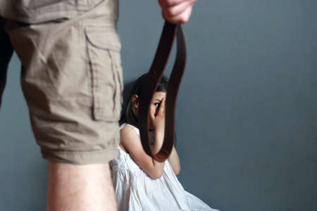 A man with a belt in his hand is going to punish a little girlの写真素材