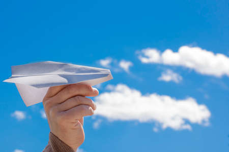 Hand of a man launching a white paper plane into the blue skyの写真素材