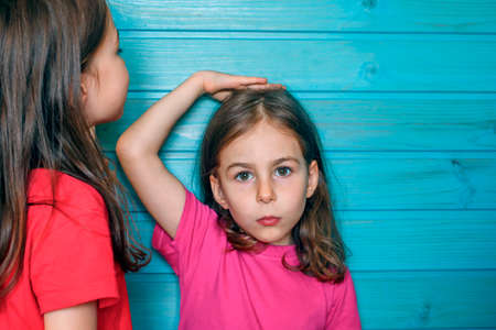 Girls measure each other's growth against a blue wooden wallの写真素材