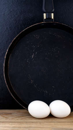 Rustic still life: a pair of eggs on a wooden table and an old frying pan hanging on the wallの写真素材