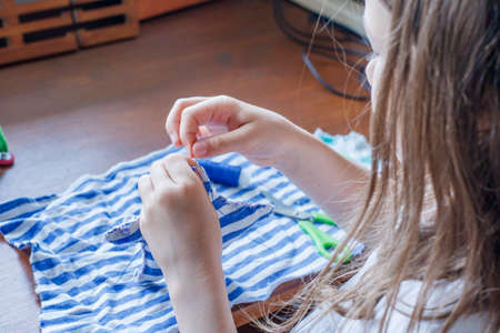 The first steps of the girl in mastering sewing. Needle with thread in the hands of the child