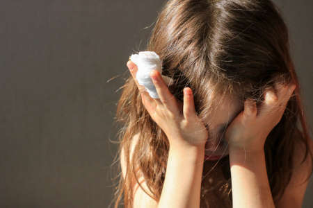 A girl with a bandaged finger cries, covering her face with her handsの写真素材