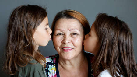 Little beautiful granddaughters kiss their beloved grandmother on both sidesの写真素材