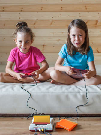 Two little sisters having fun playing video games with a joystick in their handsの写真素材