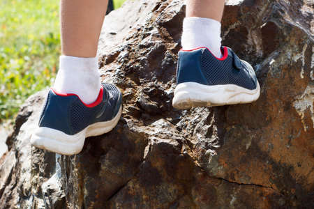 A child in blue sneakers rises up the rockの写真素材