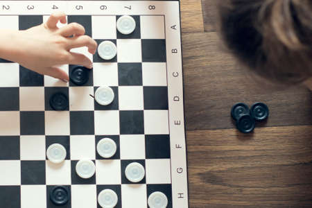 Party checkers between sisters. Toned image. Chess field. Children's tournament in checkers. Educational gamesの写真素材