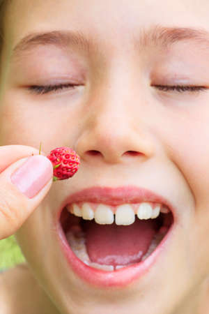 Mom puts ripe strawberries in her daughter's mouth. Season berries. Care and love