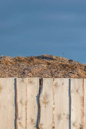 A haystack behind a wooden fence against the backdrop of a rich blue sky. Storm clouds