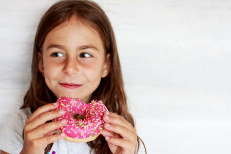 A beautiful little girl is eating a pink donut. Sweet treatの写真素材