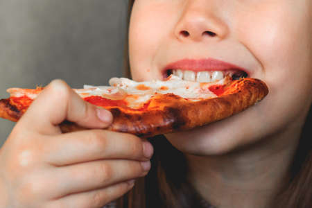 A child eats pizza with cheese and baconの写真素材
