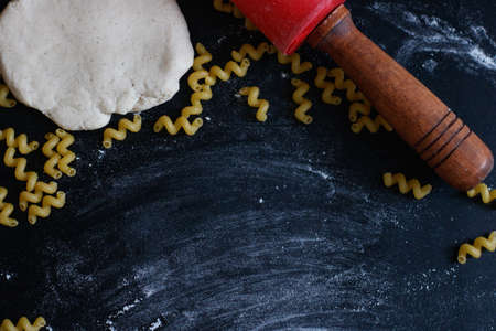 Dough, rolling pin, flour and pasta on the black table.