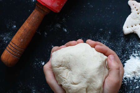 Dough in the child hands. Rolling pin, flour on the table. Top view .の写真素材