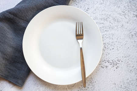 Empty white plate next to a gray kitchen towel