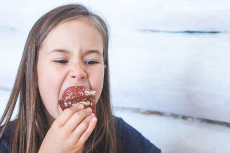 Girl eagerly eats chocolate muffin. Sugar addiction.