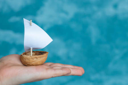 a small boat made of nutshell with a white sail in the palm of a child.の写真素材