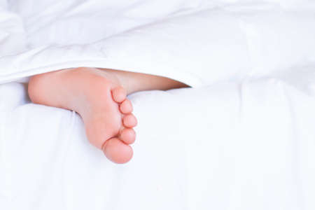Child feet under the white blanket. Tenderness of morning baby dreamの写真素材