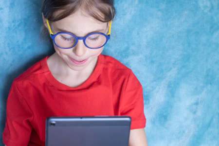 Child elementary school girl in glasses with tablet computer on distance learning. Banner templateの写真素材