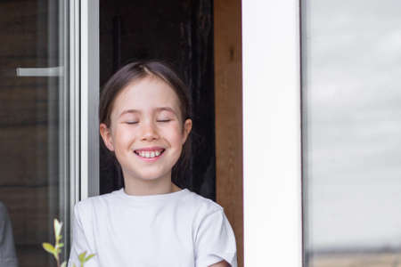 A little girl with her eyes closed enjoys the aromas of a spring day by the windowの写真素材