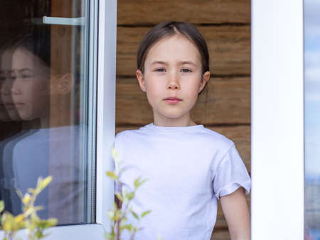 Child girl looks out the window of her apartment and enjoys the spring dayの写真素材