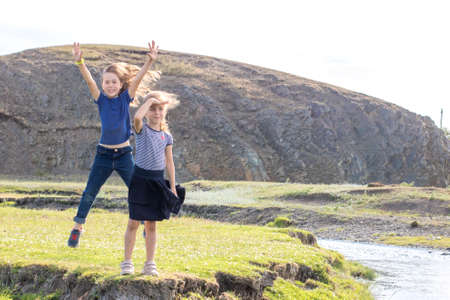 Cheerful children are jumping in the summer on the lawn by the riverの写真素材