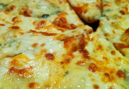 Pieces of baked appetizing pizza four cheese cooked at home on a thin dough with cheese Roquefort, Parmesan, cheddar grated, mozzarella lying on the table and shown close-upの写真素材