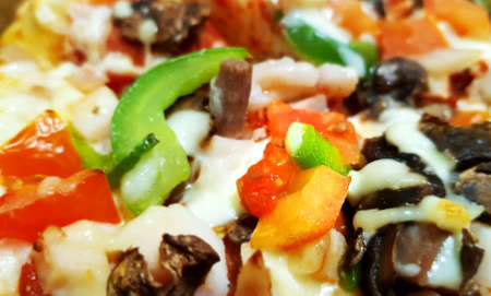 A piece of baked mouth-watering sumptuous pizzas cooked in the restaurant, the thin crust with bacon, beef, mushrooms, chicken, onions, Parmesan, pepperoni, green peppers, fresh tomatoes, pork, mozzarella cheese is on the table and shown closeupの写真素材