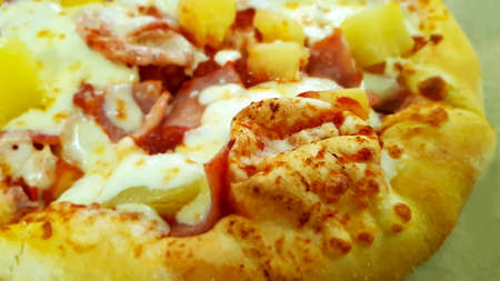 A piece of baked delicious appetizing Hawaiian pizza with ham pineapple mozzarella cheese lies on the table and is shown close-upの写真素材