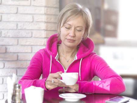 A young woman in a purple hoodie sits in a cafe and holds a white cup. Daytime, lunch, portrait, close-up, soft light. Healthy lifestyle and sports concept.の写真素材