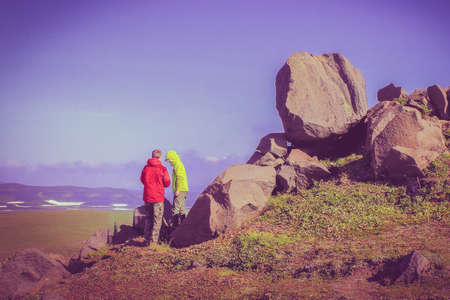 Two teenage boys in a yellow and red jacket stand back on the mountain and talk to each other. Friends went on a picnic trip. Scenic mountain scenery. Horizon. A clear summer windy day. Toned pink, purple.の写真素材