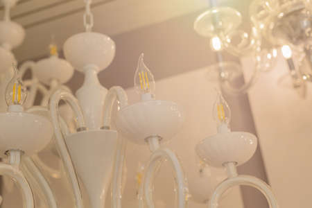 Close up on crystal of classic style chandelier, is a branched ornamental light fixture designed to be mounted on ceilings. Soft warm filter, selective focus. interior. White glossy glass.の写真素材