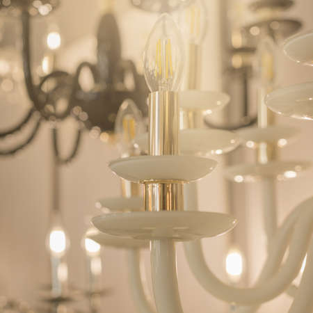 Image of a glowing chandelier with white glass fittings and candlelight shades on a gold stand. The concept of the classical style in the interior. Close up. Soft warm filter, selective focus.の写真素材