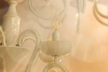 ?rystal of classic style chandelier, is a branched ornamental light fixture designed to be mounted on ceilings. Soft warm filter, selective focus. Indoor. White glossy glass.の写真素材