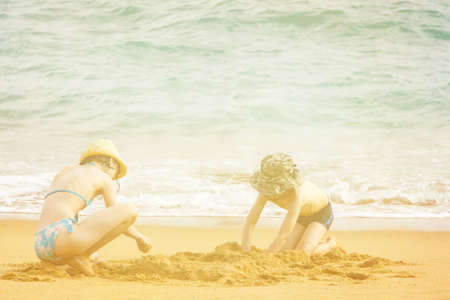Boy and girl schoolchilds sit on the coast of the sea and build a sand castle. Children play together. Friendship, nature.の写真素材