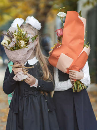 Two schoolgirls girlfriends are standing on the street hiding behind bouquets of flowers. Autumn.の写真素材