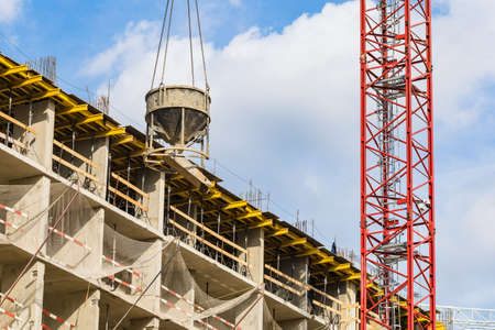 One high-rise crane with cement against a house and sky during the construction phase. Industry...