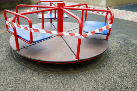 Red carousel on the playground wrapped with a barrier tape. Outdoors. Prohibition of outdoor walks, prevention of the biological hazard of the coronavirus influenza virus covid-19. playground parkの写真素材